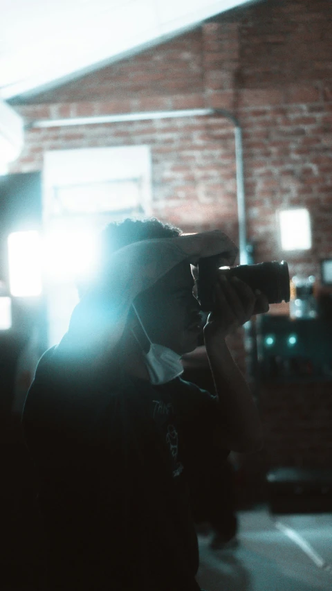 a man holding a camera in front of a building, by Robbie Trevino, standing in a dimly lit room, anamorphic lens flares, high quality photo, facing away from camera