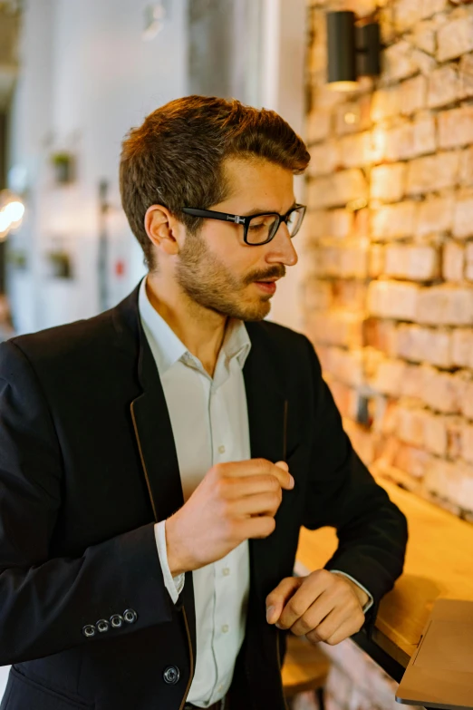 a man standing in front of a laptop computer, by Mathias Kollros, pexels contest winner, wearing a blazer, jewish young man with glasses, standing in a restaurant, thoughtful )