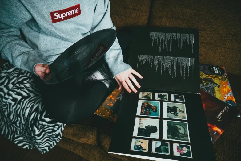 a person sitting on a couch holding a hat, an album cover, unsplash, visual art, supreme, yeezy collection, old photobook, 268435456k film