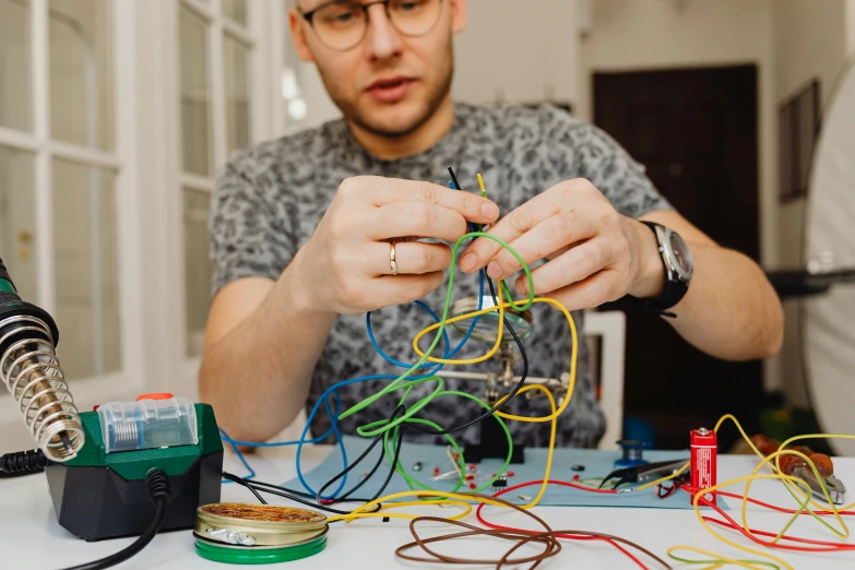 a man sitting at a table working on wires, trending on pexels, process art, school curriculum expert, abstract claymation, hipster dad, electronics see through