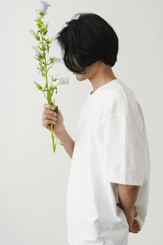 a person holding a flower in front of a white background, by Miyamoto, unsplash, dressed in a white t shirt, style of yoshii chie, ignant, 165 cm tall