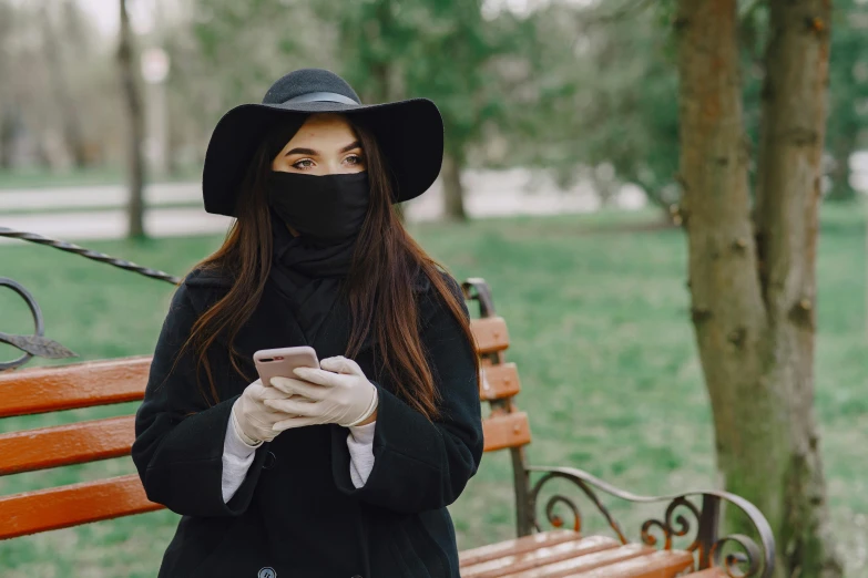 a woman sitting on a park bench looking at her phone, by Julia Pishtar, trending on pexels, happening, plague doctor mask, square, anastasia ovchinnikova, wearing black