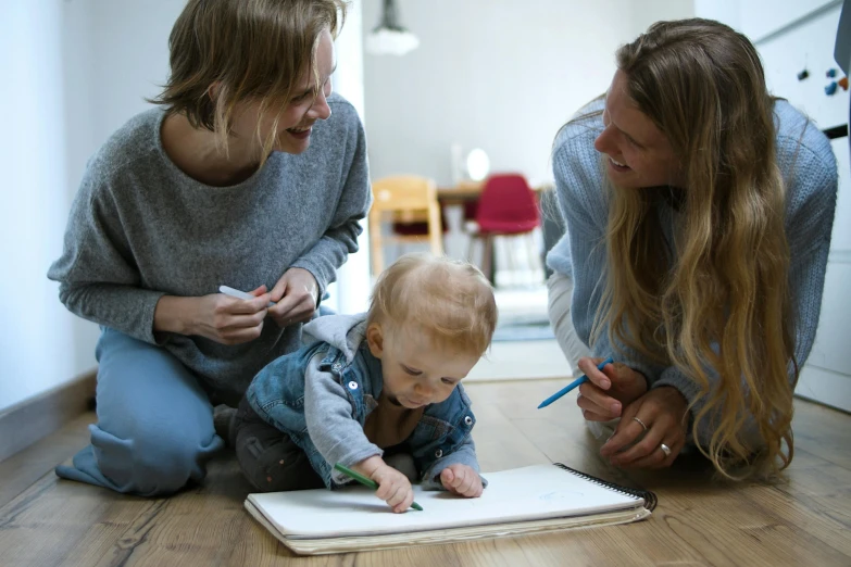 two women and a baby are sitting on the floor, a child's drawing, pexels contest winner, on a coffee table, blonde, drawing sketches on his notebook, super high resolution