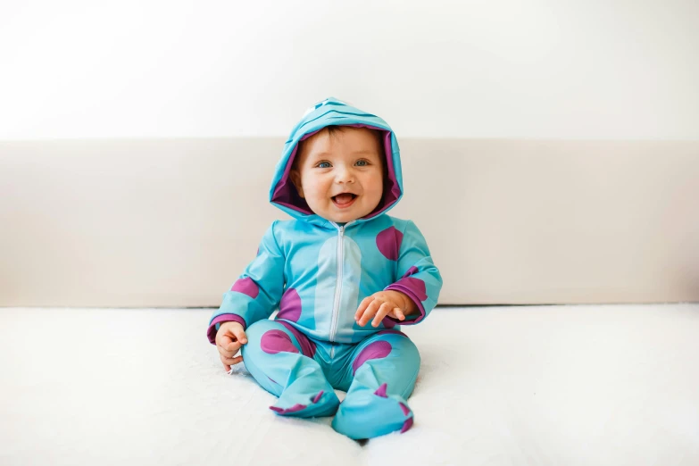 a baby sitting on top of a white couch, by Joe Bowler, unsplash, wearing hero costume, blue and purple colour scheme, turquoise, wearing a tracksuit