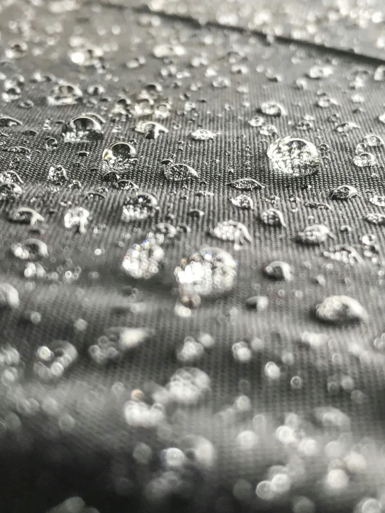 a black and white photo of water droplets on a cloth, sleek waterproof design, visible stitching, up-close, mesh fabrics