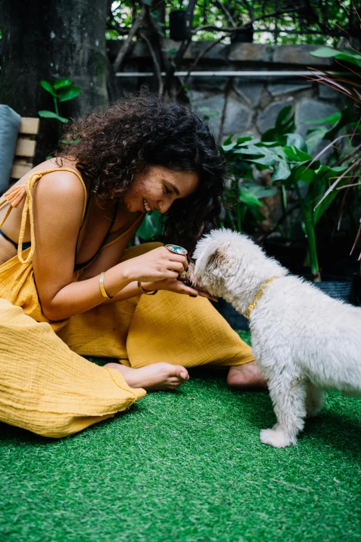 a woman in a yellow dress playing with a white dog, pexels contest winner, lush garden surroundings, snacks, australian, nathalie emmanuel