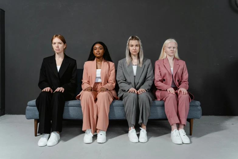 a group of women sitting on top of a blue couch, trending on pexels, aestheticism, wearing black grey suit, wearing a light - pink suit, wearing white sneakers, professional image