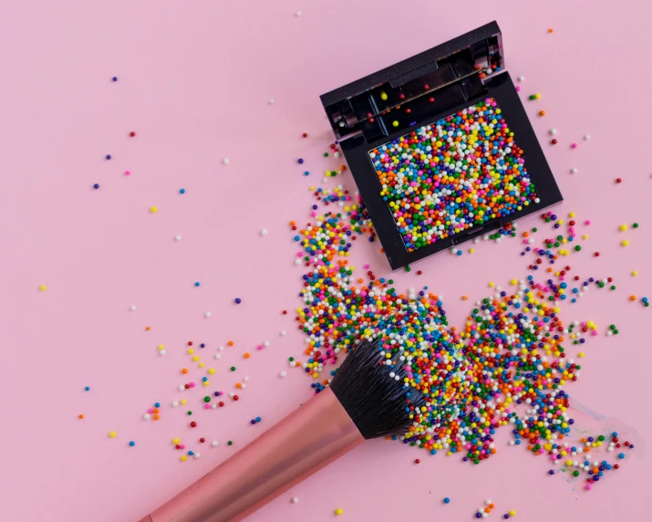 a brush and sprinkles on a pink background, trending on pexels, pointillism, unreal engine : : rave makeup, multicoloured, miniature product photo, black eyeshadow