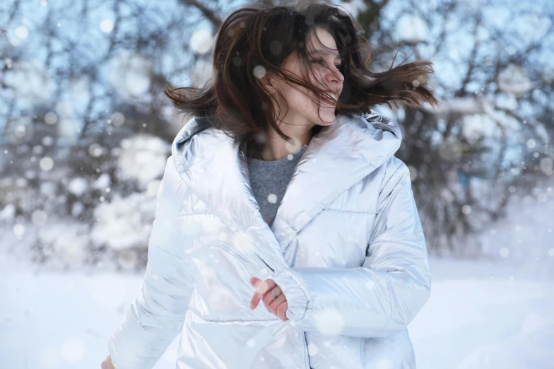 a woman standing in the snow with her hair blowing in the wind, pexels contest winner, silver metallic moncler jacket, smiling and dancing, avatar image, brunette