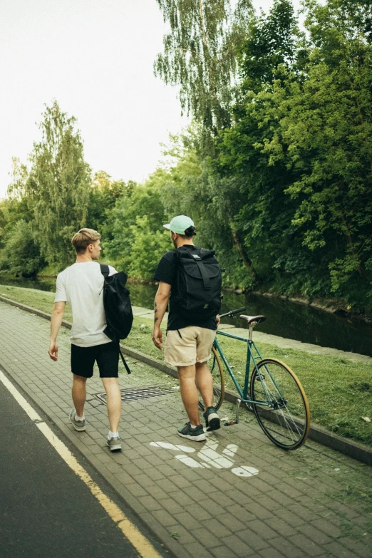 a couple of men walking down a street next to a river, pexels contest winner, wearing black shorts, wide greenways, college students, riding
