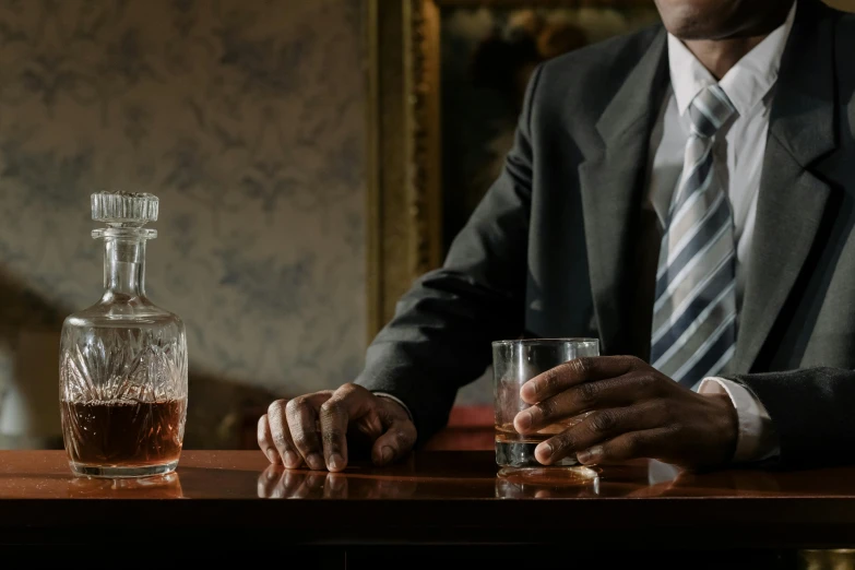 a man in a suit sitting at a bar, a portrait, inspired by William Grant Stevenson, pexels contest winner, renaissance, whiskey bottle, black man, william eggleston style, thumbnail