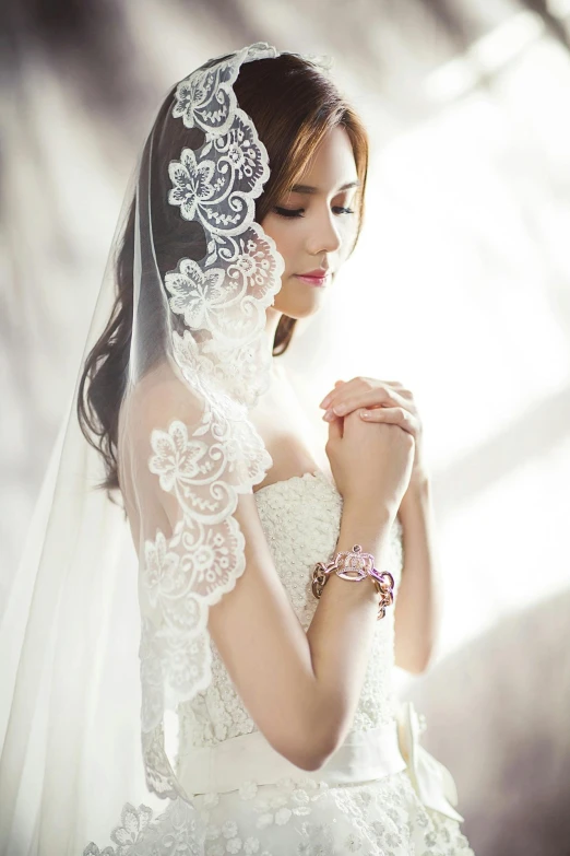 a woman in a wedding dress holding her hands together, looking off to the side, veils and jewels, tiffany style, an asian woman