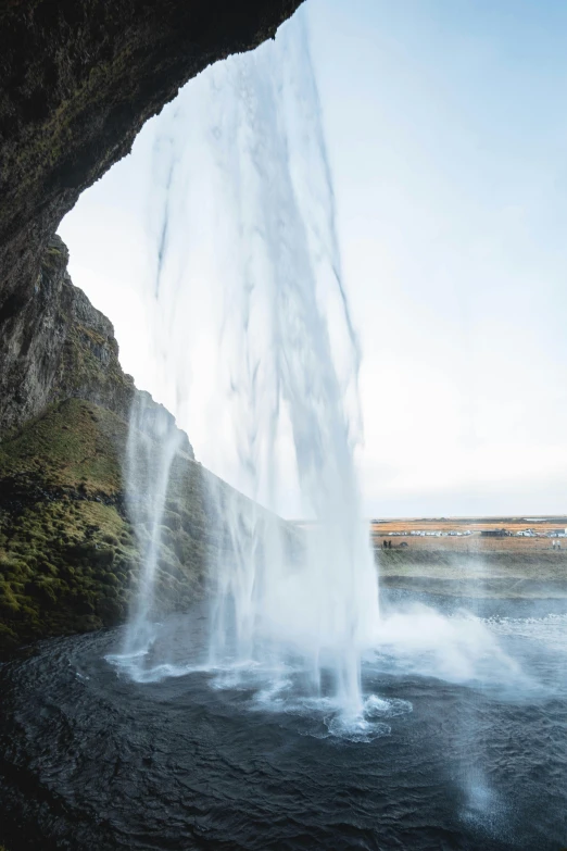 a waterfall coming out of a cave into a body of water, iceland hills in the background, water jets, unsplash photo contest winner, fall season