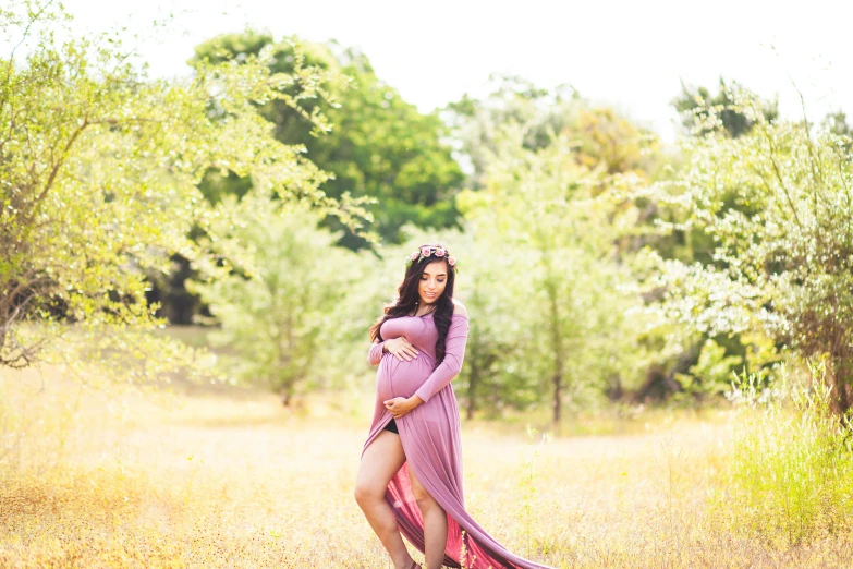 a pregnant woman in a purple dress standing in a field, unsplash, draped in pink and green robes, alanis guillen, casual pose, fall season