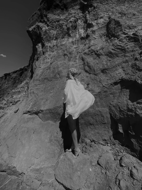 a black and white photo of a person standing on a rock, a black and white photo, by Alexis Grimou, surrealism, nico wearing a white dress, wearing desert poncho, 15081959 21121991 01012000 4k, beth cavener