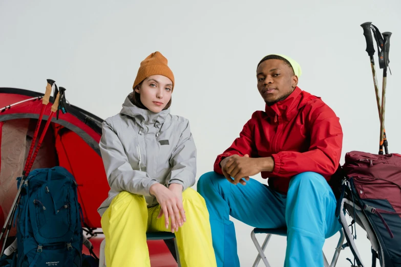 a couple of people sitting next to each other, inspired by Salomon van Abbé, trending on pexels, renaissance, bright trouser suit for a rave, camping, payne's grey and venetian red, college students