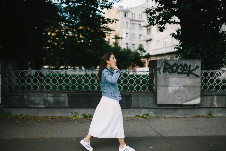 a woman walking down a street talking on a cell phone, by Emma Andijewska, pexels contest winner, happening, white skirt, denim jacket, running pose, modest