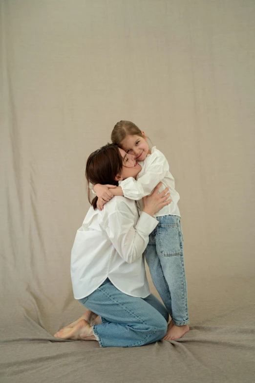 a woman hugging a little girl on top of a bed, by Attila Meszlenyi, pexels contest winner, white shirt and jeans, in front of white back drop, softplay, shirt