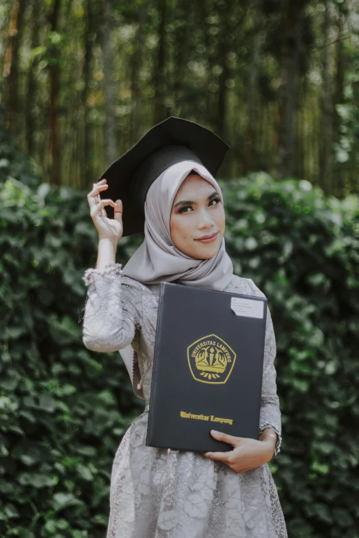 a woman in a graduation gown holding a book, by Basuki Abdullah, pexels contest winner, wearing a light grey crown, instagram post, ((portrait)), vp of marketing