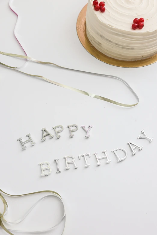 a birthday cake sitting on top of a table, inspired by Cerith Wyn Evans, letterism, silver，ivory, medium close up, ribbon, product shot