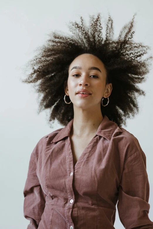 a woman standing in front of a white wall, a character portrait, pexels contest winner, black arts movement, frizzy hair, portrait sophie mudd, wearing a linen shirt, riyahd cassiem