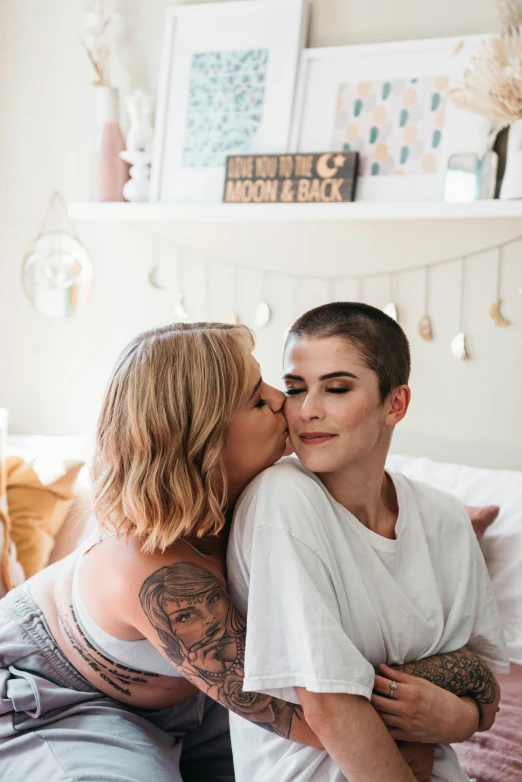 a woman sitting on top of a bed next to a man, a photo, by Jessie Alexandra Dick, trending on pexels, lesbian embrace, brown buzzcut, portrait of two girls kissing, katey truhn