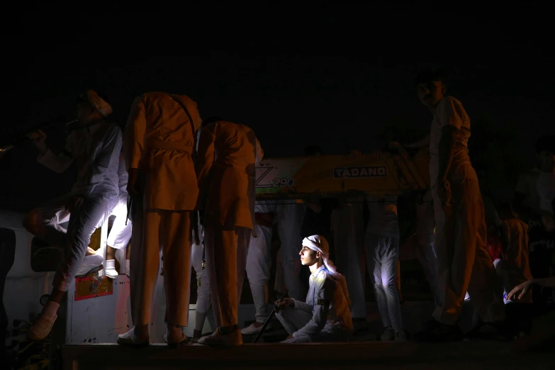 a group of people that are standing in the dark, white uniform, lamps on ground, india, ignant