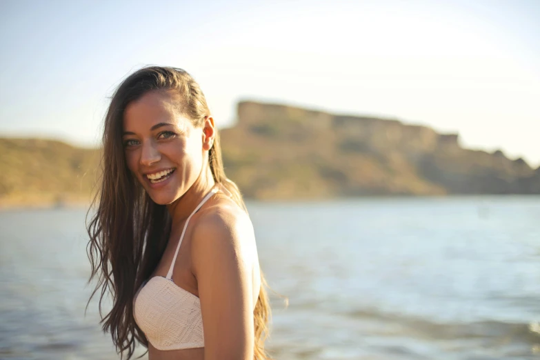 a beautiful young woman standing next to a body of water, cheeky smile, slightly tanned, profile image, goofy smile