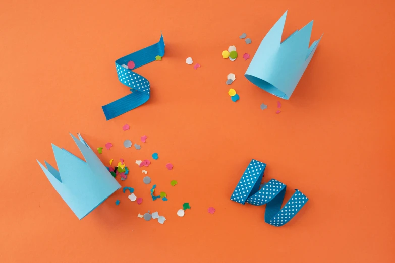 paper crowns and confetti sprinkles on an orange background, by Helen Stevenson, with a blue background, spiked wristbands, papercraft, top hats