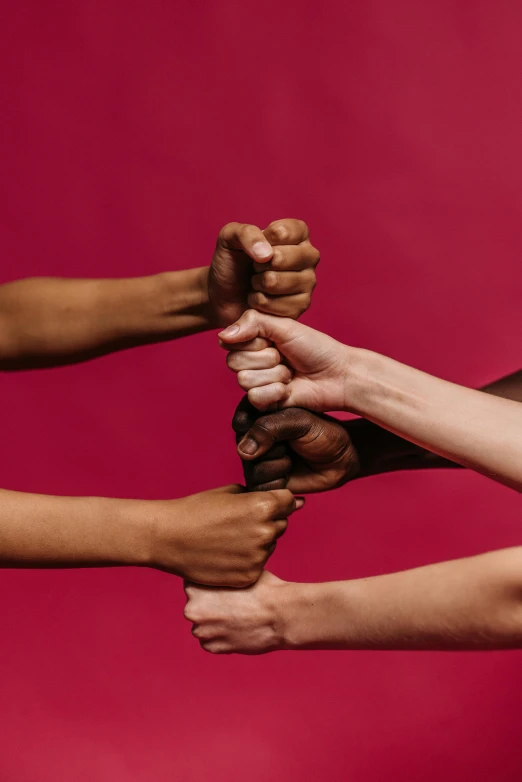 a group of people holding their hands together, by Arabella Rankin, on a red background, fist training, women fighting men, varying ethnicities