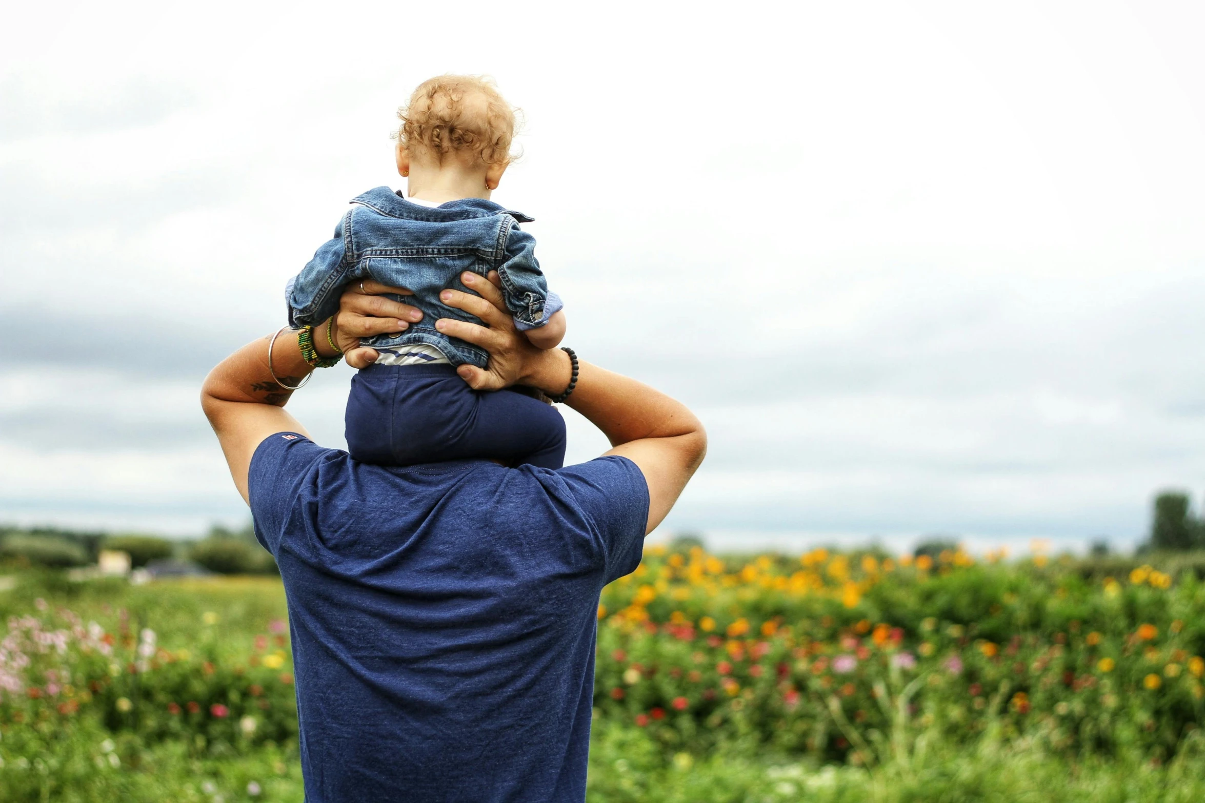 a man holding a small child in his arms, pexels, field of dreams, back towards camera, various posed, overlooking