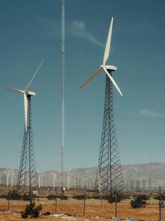 a group of wind turbines sitting on top of a dry grass field, a colorized photo, by Jacob Burck, unsplash contest winner, palm springs, medium shot of two characters, high detail 4 k, tall structures