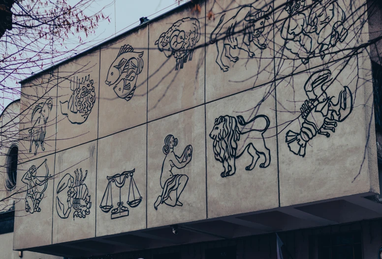 a building with a mural on the side of it, a cartoon, by Julia Pishtar, trending on pexels, street art, zodiac libra sign, etched relief, panel of black, pyrography