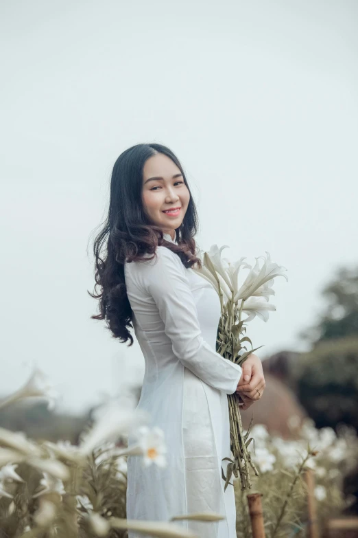 a woman standing in a field holding a bunch of flowers, inspired by Cui Bai, pexels contest winner, ao dai, white, square, portait image