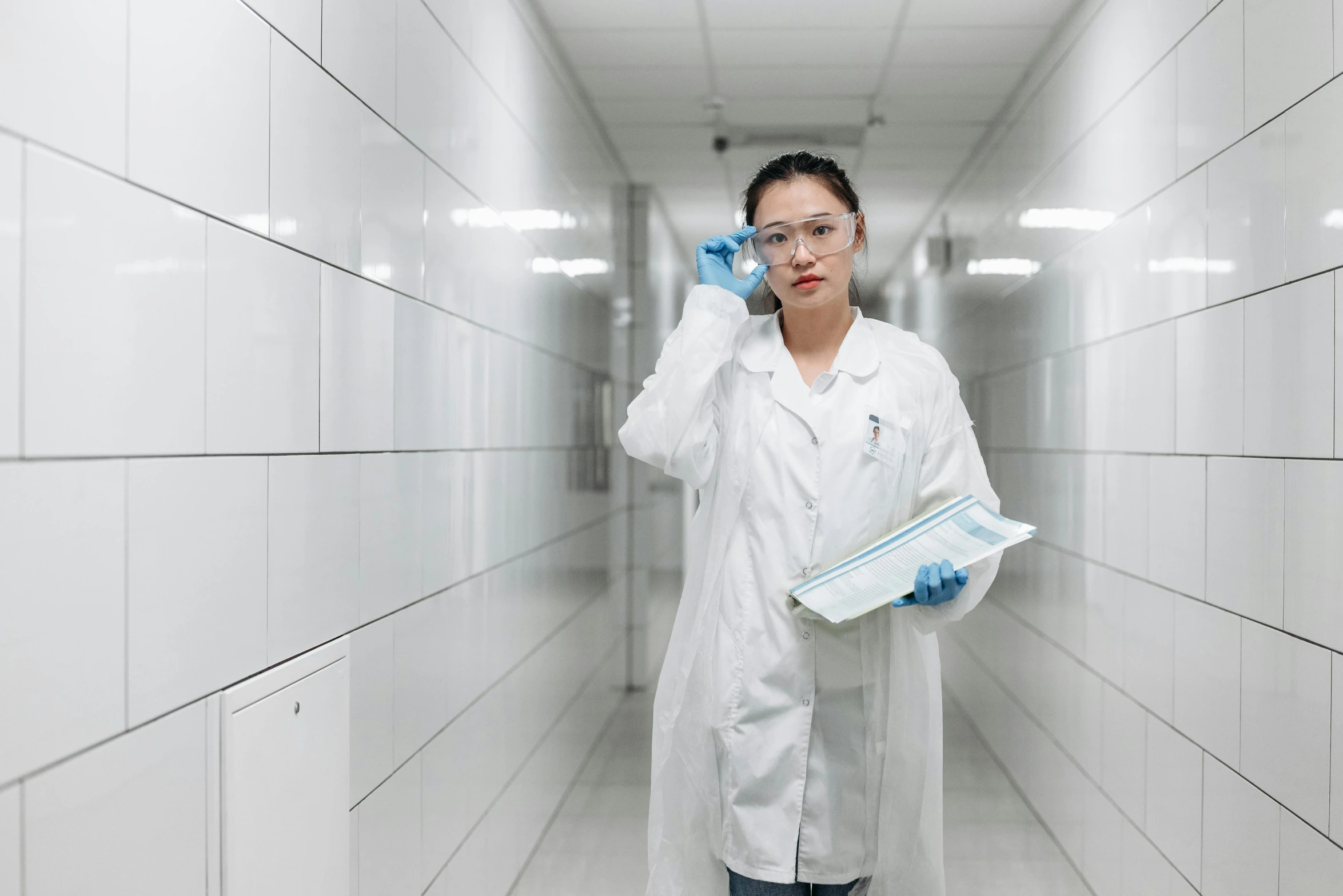 a woman in a lab coat talking on a cell phone, by Andries Stock, pexels contest winner, sterile minimalistic room, bo chen, holding a clipboard, wearing gloves
