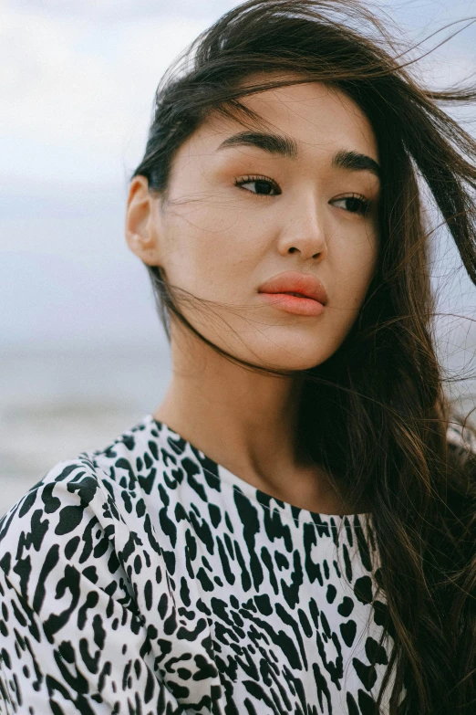 a woman standing on top of a beach next to the ocean, inspired by Tadashi Nakayama, trending on pexels, detailed face of a asian girl, patterned clothing, sharp cheekbones, beans