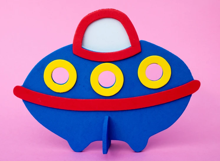 a toy shaped like a submarine on a pink background, inspired by Eduardo Paolozzi, unsplash, pop art, key hole on blue ball, wooden hippo, ufo, circular cardboard eyes