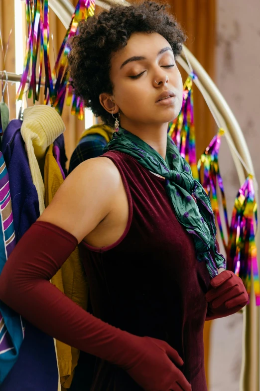 a woman standing in front of a rack of clothes, jewel tones, wrapped arms, thoughtful, over-shoulder shot