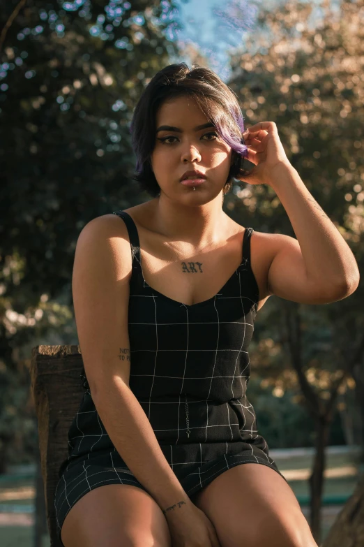 a woman sitting on a bench talking on a cell phone, a tattoo, inspired by Elsa Bleda, trending on pexels, wearing black camisole outfit, south east asian with round face, woman posing, sitting on a tree