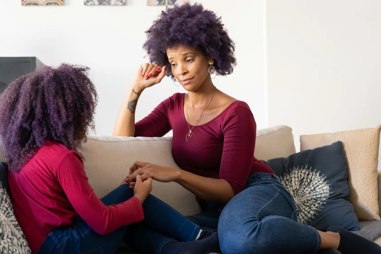 two women sitting on a couch talking to each other, by Everett Warner, pexels, antipodeans, purple outfit, with a kid, natural hair, she's sad