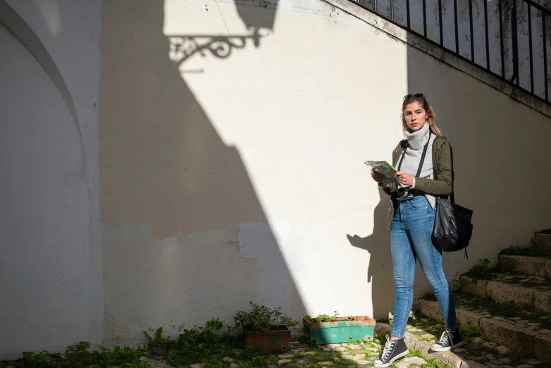 a woman standing in front of a white wall, by Julian Allen, realism, dappled afternoon sunlight, college students, european woman photograph, reading