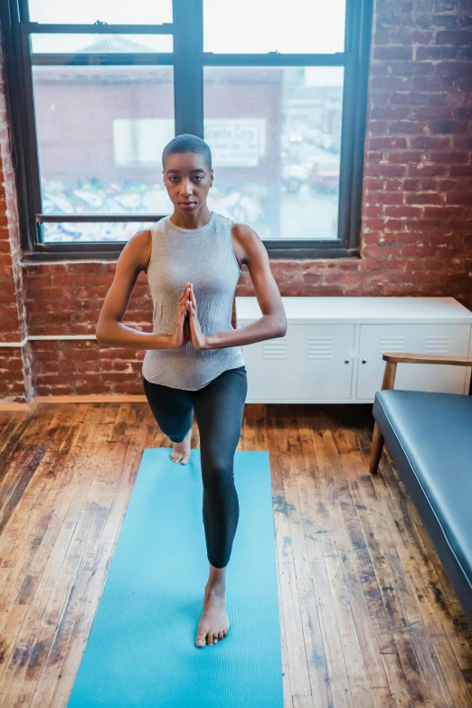 a woman standing on a yoga mat in front of a window, jemal shabazz, low quality photo