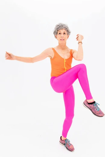 a woman in a bright orange top and pink leggings, jumping at the viewer, 7 0 years old, spoon slim figure, threatening pose