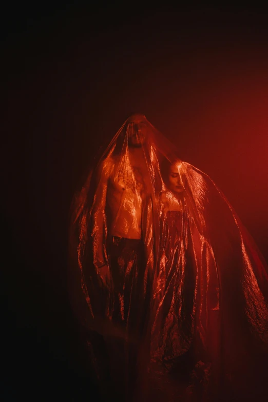 a person standing in front of a red light, diaphanous iridescent cloth, cloaked woman, wet fabric, gold and red metal