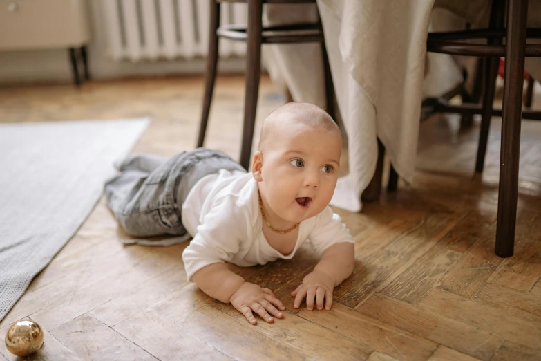 a baby laying on the floor next to a christmas ornament, by Emma Andijewska, pexels contest winner, happening, hardwood floor boards, looking surprised, gif, vin diesel with a tummy