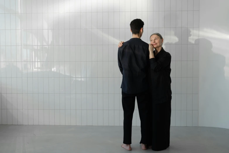 a woman standing next to a man in a bathroom, inspired by Fei Danxu, unsplash, conceptual art, wearing black robes, in front of white back drop, holding each other, ren xun and maruyama ōkyo