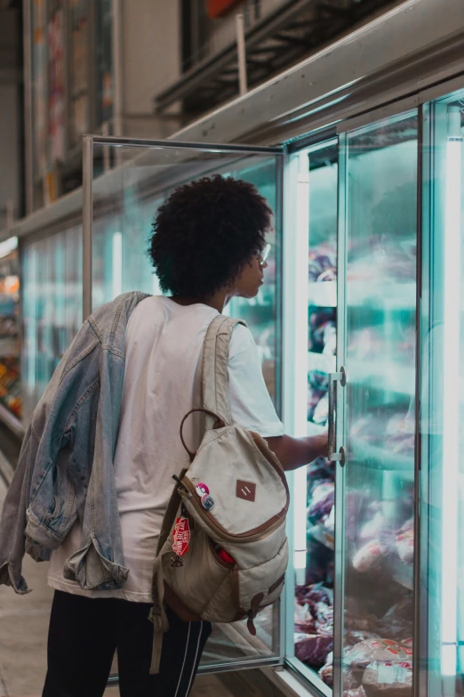 a woman standing in front of a display case filled with donuts, trending on pexels, happening, refrigerated storage facility, black young woman, backlit shot girl in parka, getting groceries