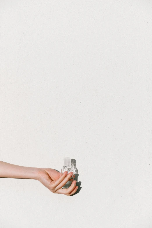 a person holding a piece of paper in their hand, inspired by Ren Hang, trending on pexels, carrying a bottle of perfume, unsplash transparent, white wall, cassette