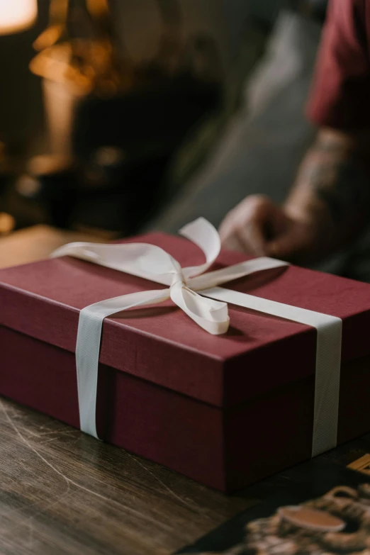 a red gift box sitting on top of a wooden table, pexels contest winner, maroon and white, manly, ribbon, woman