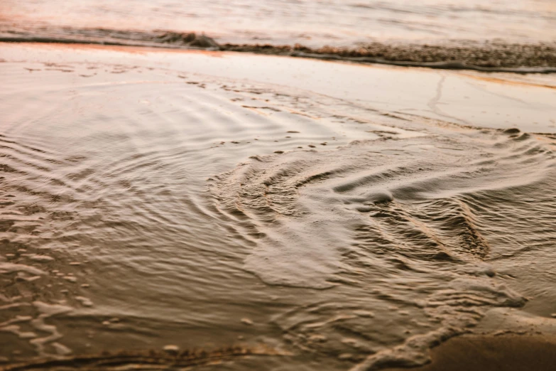 a couple of footprints in the sand at the beach, unsplash, australian tonalism, water swirling, brown, honey ripples, early evening